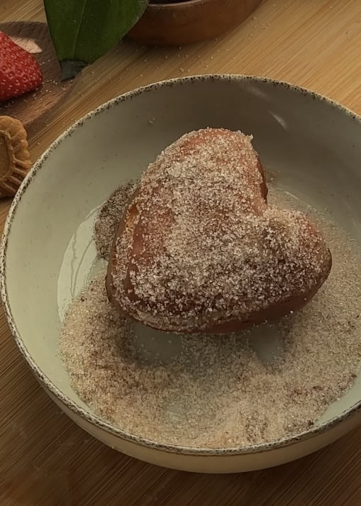 Coating a heart-shaped Nutella donut with sugar and cinnamon mixture for a sweet finish.
