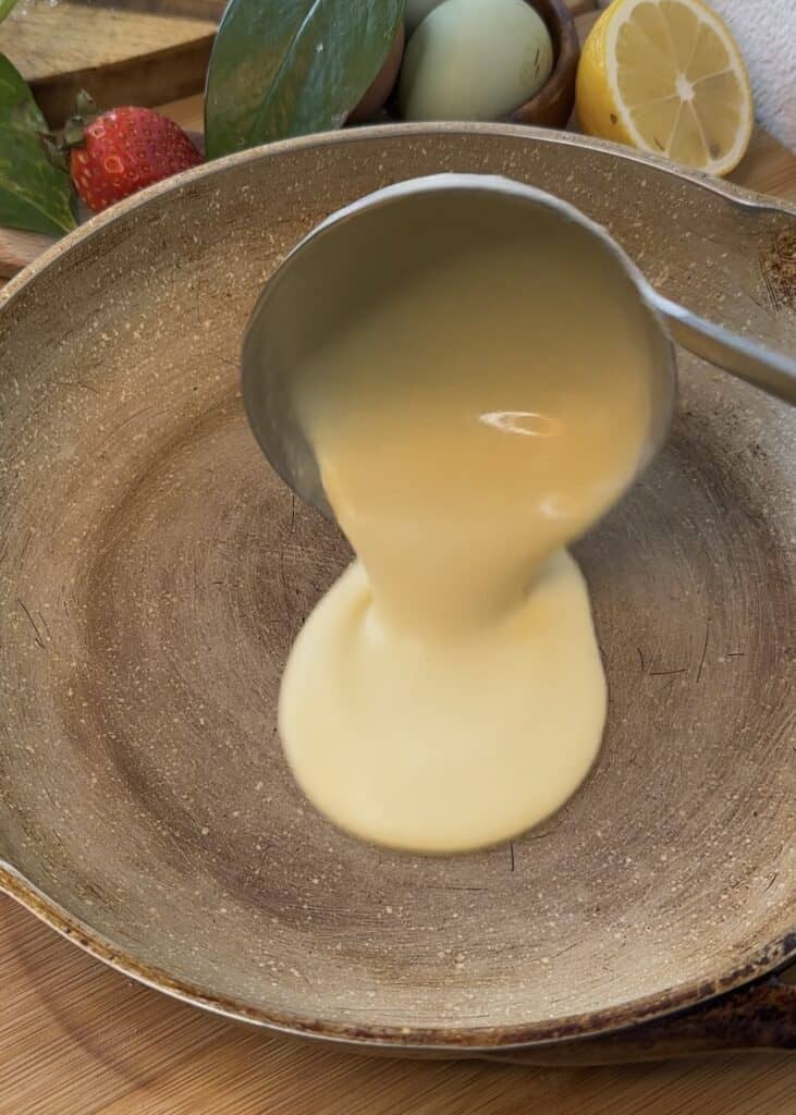 Pouring crepe batter into a hot pan and tilting it to spread the batter evenly for making Nutella crepe rolls.
