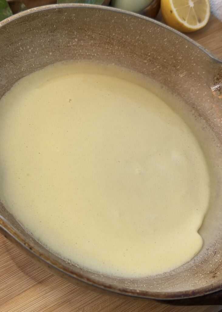 Tilting the pan to spread crepe batter evenly for thin and perfectly cooked crepes used in Nutella crepe rolls.