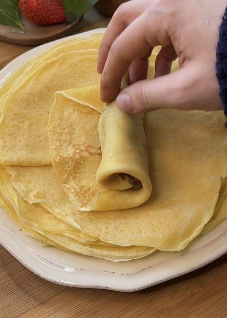Rolling a Nutella-filled crepe into a tight roll to create Nutella crepe rolls