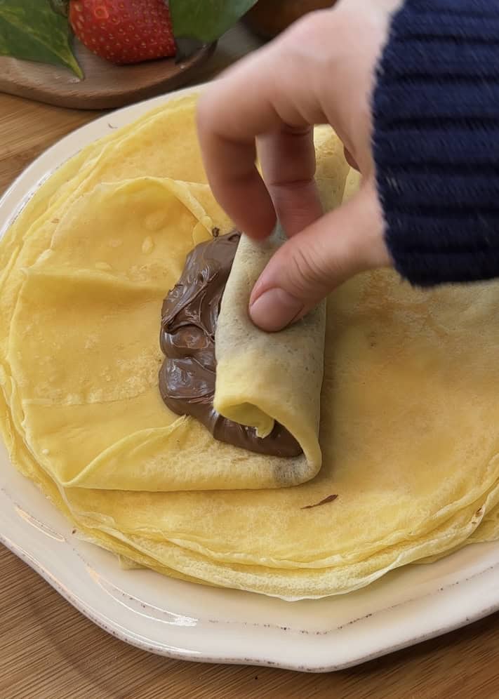 Rolling a Nutella-filled crepe into a tight roll to create Nutella crepe rolls