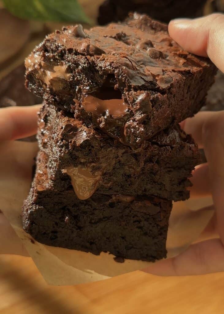 A stack of three fudgy brownies with gooey chocolate oozing from the center, perfect for chocolate lovers and homemade dessert enthusiasts.