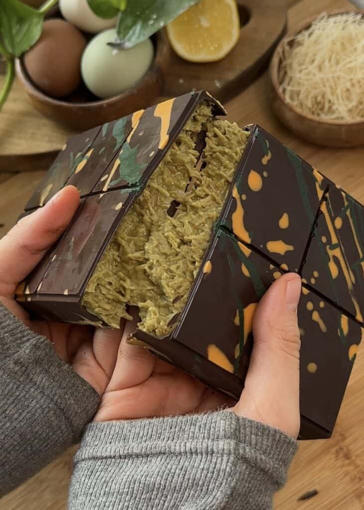 Homemade Dubai chocolate bar cut in half, showing layers of crunchy kataifi pastry and creamy pistachio filling, topped with rich chocolate.