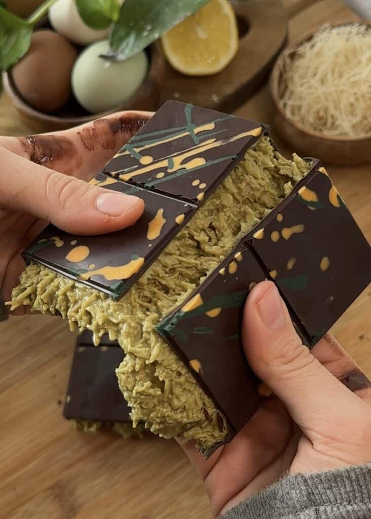 Homemade Dubai chocolate bar cut in half, showing layers of crunchy kataifi pastry and creamy pistachio filling, topped with rich chocolate.