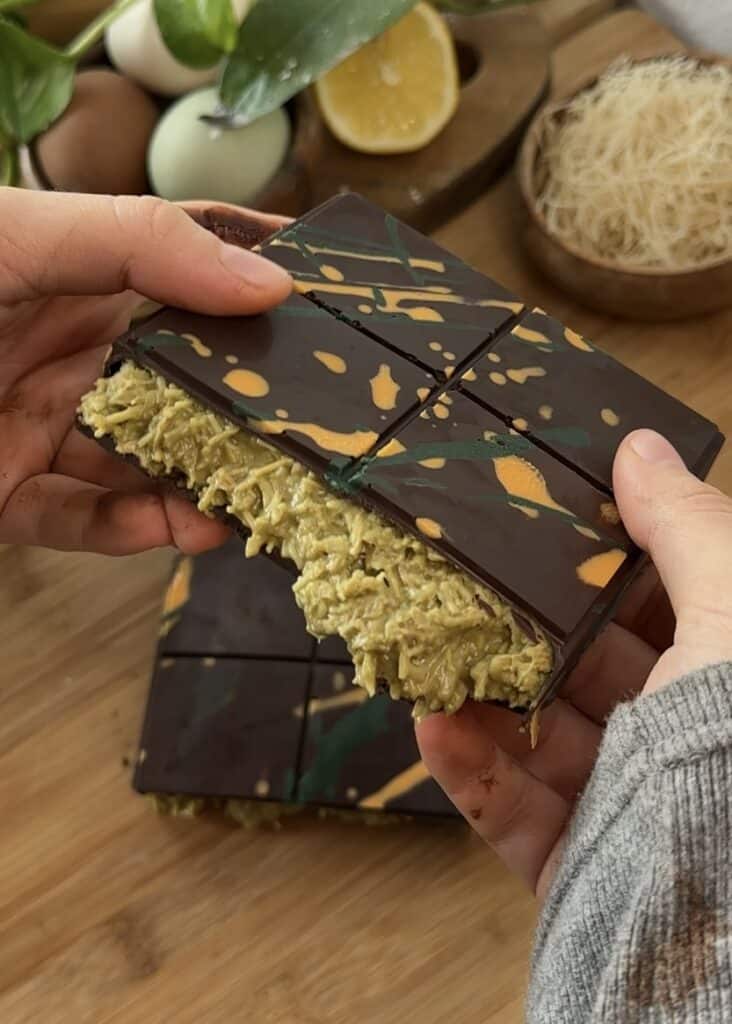 Homemade Dubai chocolate bar cut in half, showing layers of crunchy kataifi pastry and creamy pistachio filling, topped with rich chocolate.