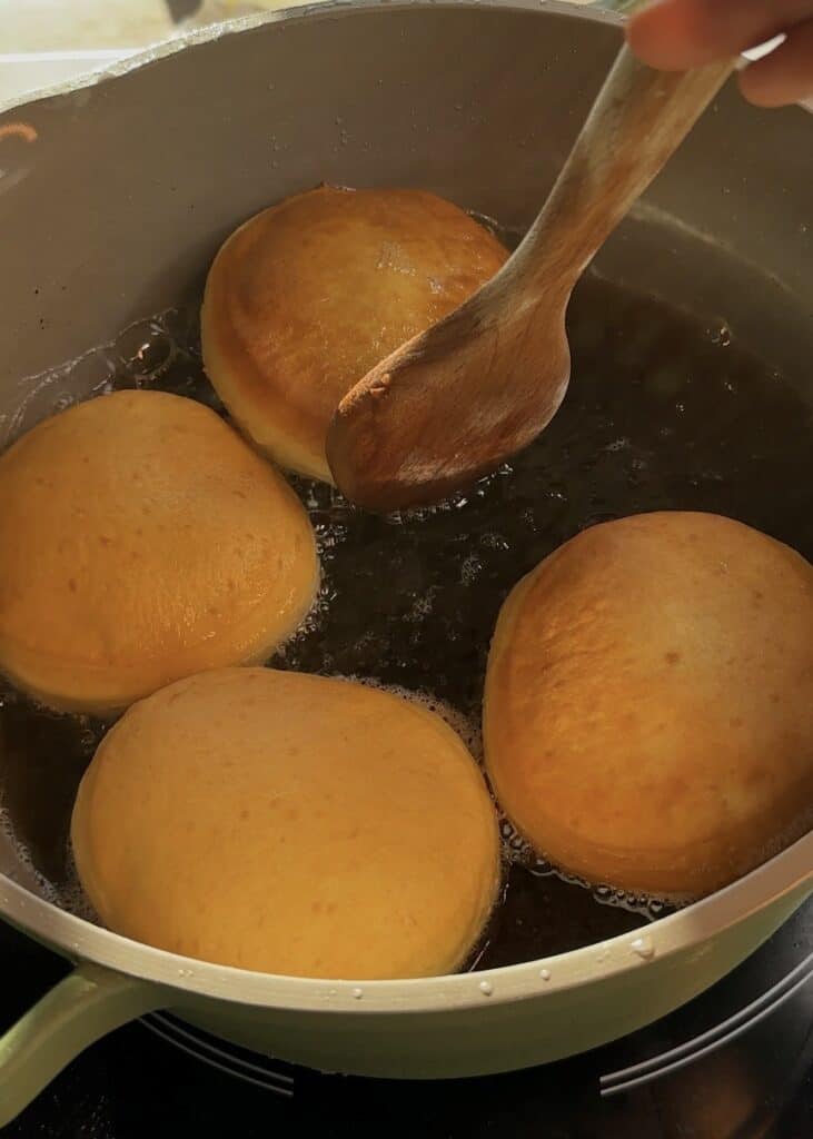 Pistachio donuts frying in hot oil, turning golden brown.