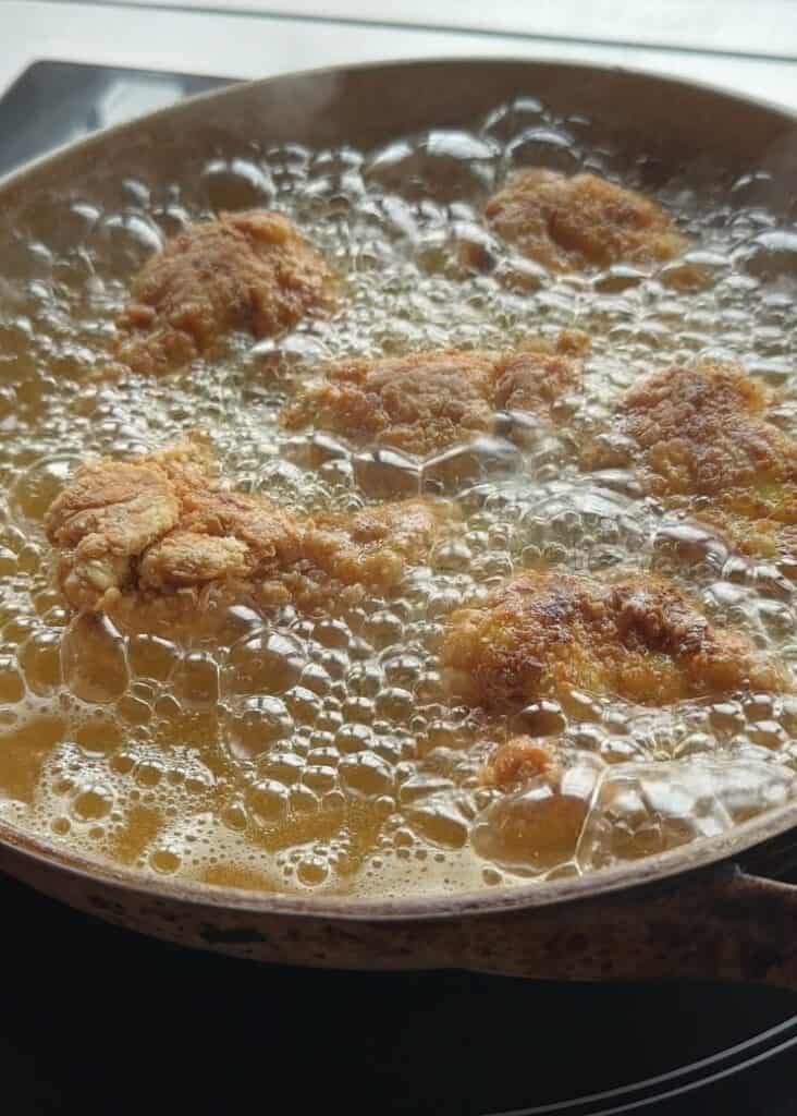 Chicken drumsticks frying in hot oil, bubbling and turning golden brown, creating a crispy exterior.