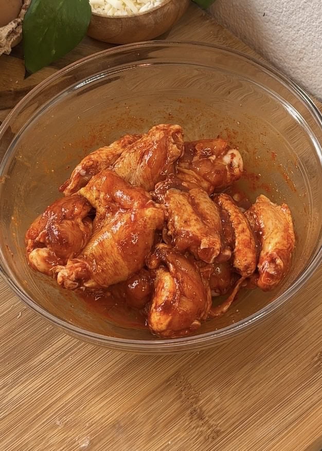 Chicken wings coated in spices and egg in a mixing bowl, ready to be fried for crispy garlic Parmesan wings.