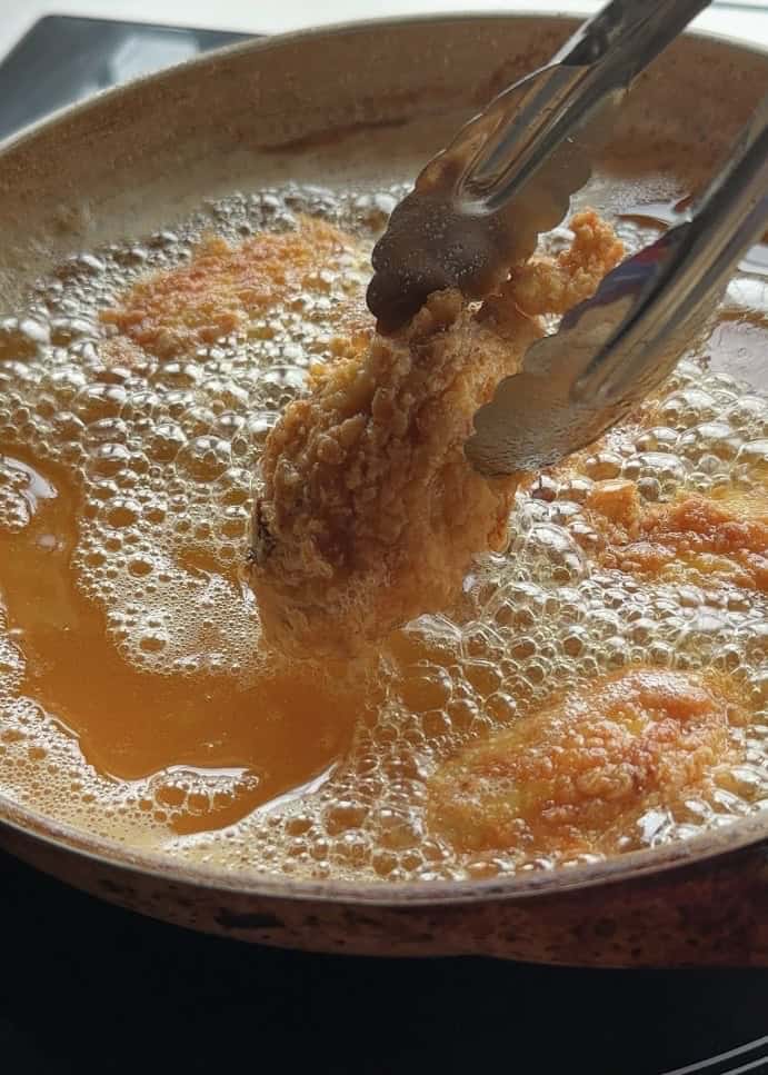 A golden-brown chicken wing lifted from hot oil with tongs, showcasing its crispy, perfectly fried exterior.