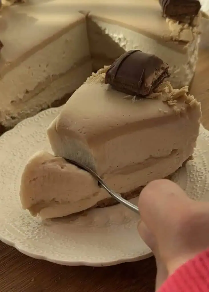 Spooning the first bite of a no-bake Kinder Bueno cheesecake, showcasing its creamy texture and rich flavors.