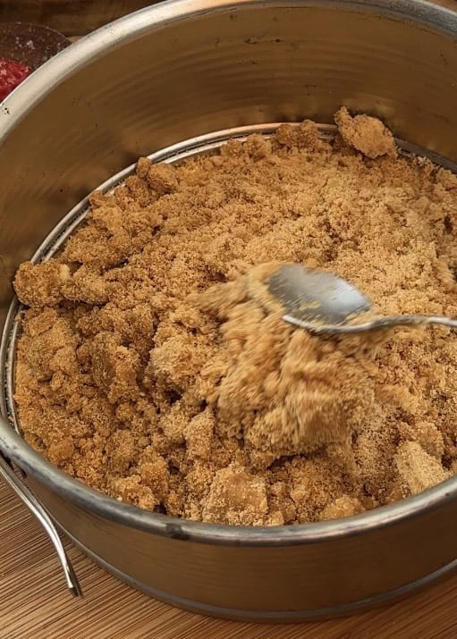 Pressing a mixture of crushed cookies and butter into a pan to create the base for a no-bake Kinder Bueno cheesecake.