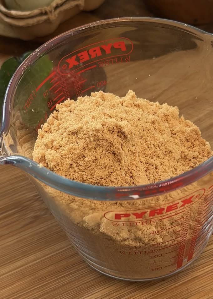 Crushed biscuits in a Pyrex dish, ready to be pressed into the base for a no-bake Kinder Bueno cheesecake.