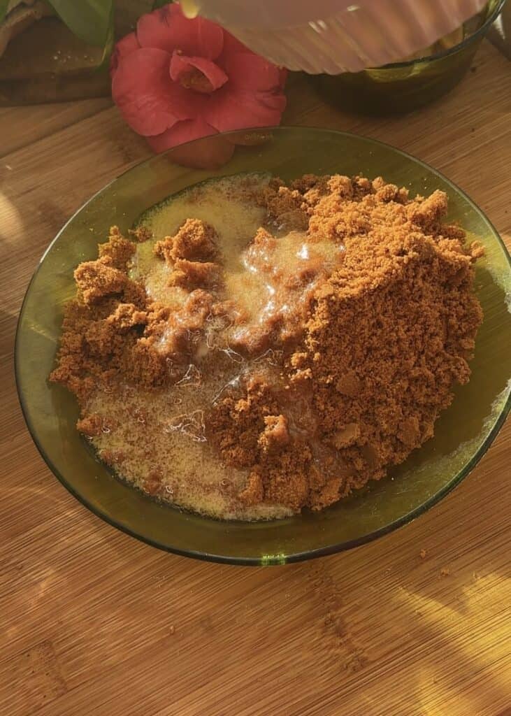 Mixing crushed biscuits with melted butter in a green plate for No-Bake Apple Pie Cheesecake with Crumble.