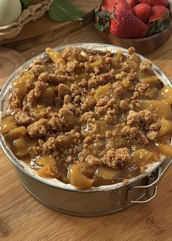 No bake apple pie cheesecake with crumble, featuring a crunchy crumble base, smooth cheesecake filling, spiced, saucy apples in the middle and on top, finished with a layer of crumble.