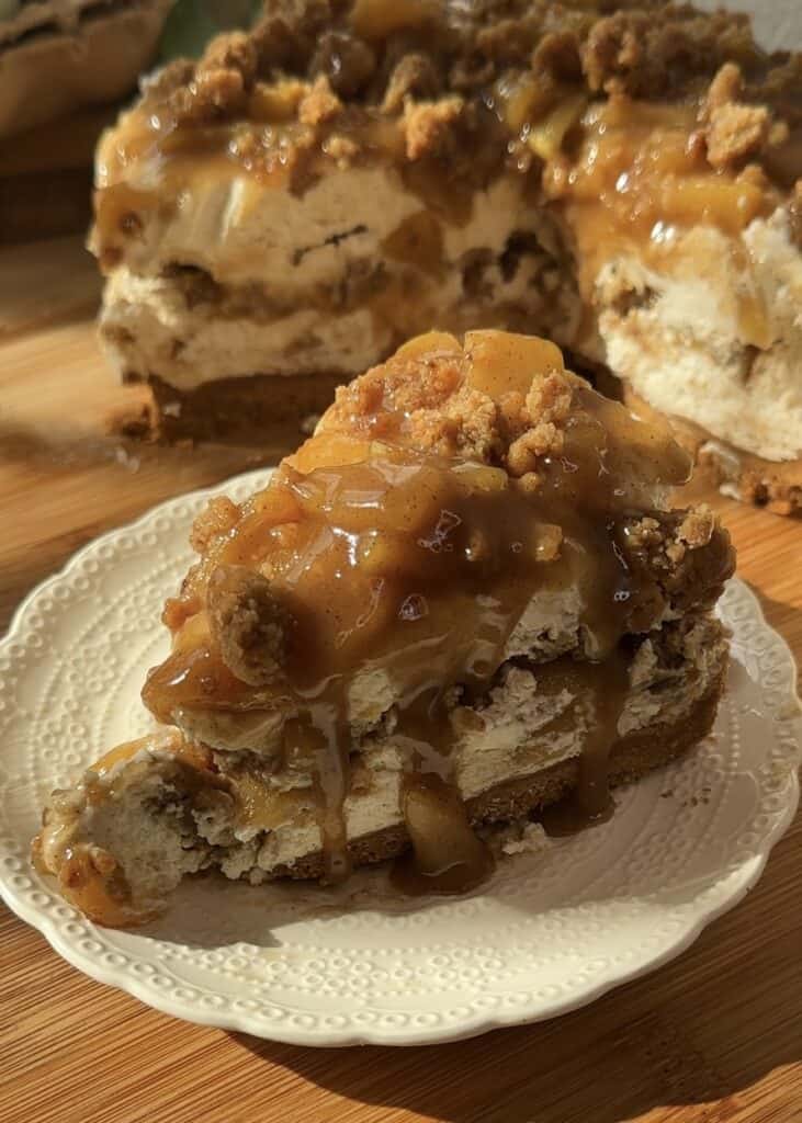A slice of no-bake apple pie cheesecake with crumble, featuring a crunchy crumble base, smooth cheesecake filling, spiced saucy apples in the middle, and topped with more saucy apples and crumble.