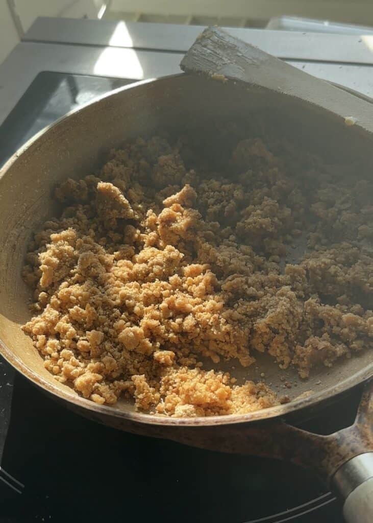 Cooking crumble in a pan over medium heat, stirring constantly to prevent burning for No-Bake Apple Pie Cheesecake with Crumble.