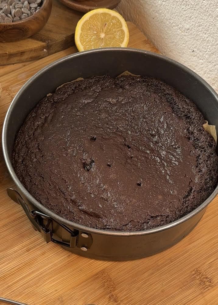 A greased mold with baking paper, filled with rich chocolate cake that has been baked for the base of a milk chocolate mousse cake.