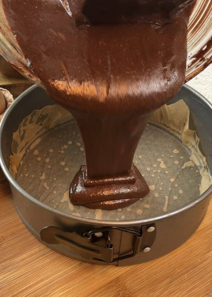 Pouring chocolate cake batter into a greased mold with baking paper to bake the base for a milk chocolate mousse cake.