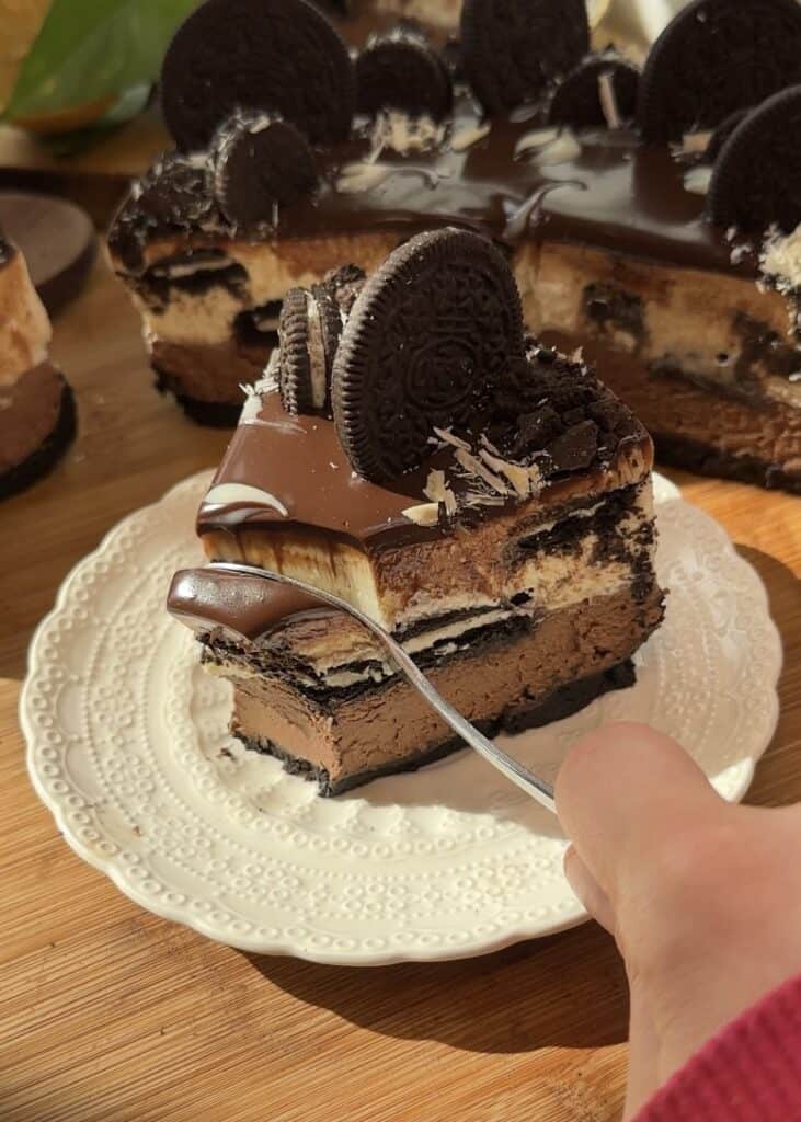 Indulgent second bite of a creamy no-bake chocolate Oreo cheesecake with rich chocolate layers, an Oreo crust, and a decadent ganache topping with Oreo cookies and white chocolate shavings.