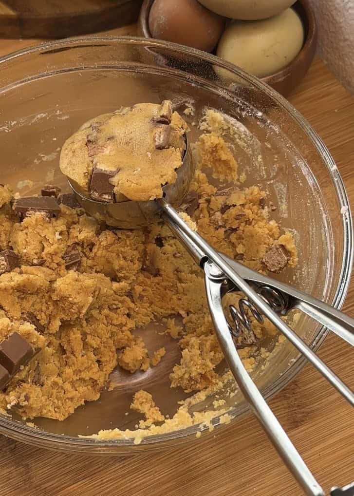 Scooping Copycat Crumbl KitKat cookie dough onto a tray using an ice cream scoop before freezing for perfect texture.
