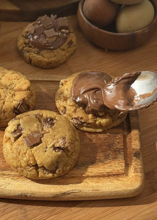 Homemade Copycat Crumbl KitKat cookies with a gooey texture, KitKat pieces inside, a rich chocolate spread on top, and extra KitKats for decoration.