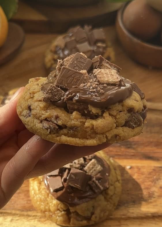 Homemade Copycat Crumbl KitKat cookies with a gooey texture, KitKat pieces inside, a rich chocolate spread on top, and extra KitKats for decoration.