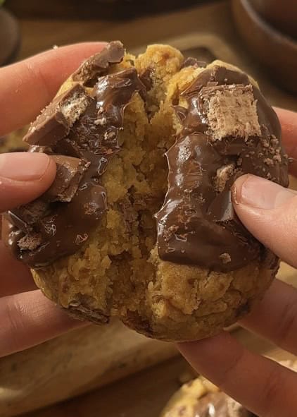 Half of a Copycat Crumbl KitKat cookie, revealing its gooey, chocolatey interior with melted KitKat pieces inside, topped with a rich chocolate spread and extra KitKats for decoration.
