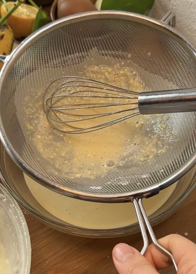 Straining crepe batter through a sieve to ensure a smooth, lump-free consistency, prepared on a rustic wooden table