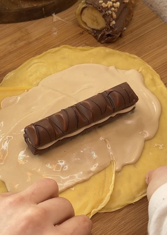 Rolling sushi crepes filled with Kinder Bueno spread and whole Kinder Buenos, prepared on a rustic wooden table, ready for decoration