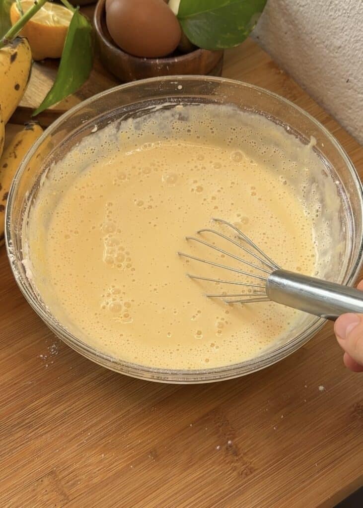 Mixing crepe batter in a glass bowl with a whisk until smooth and homogeneous