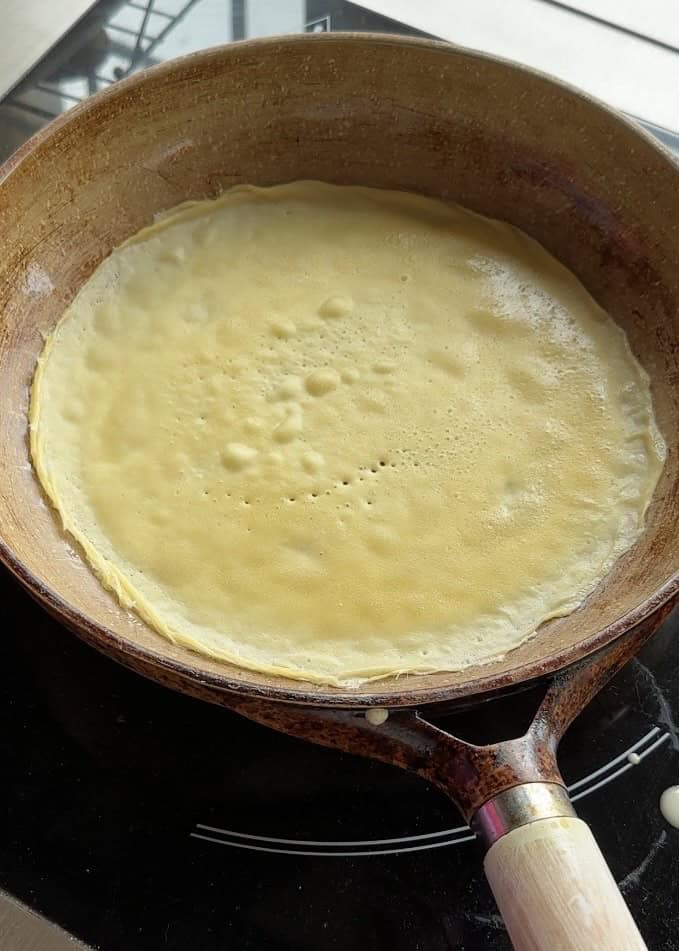Cooking thin crepes in a wide cooking pan, spreading the batter evenly for a perfect golden texture