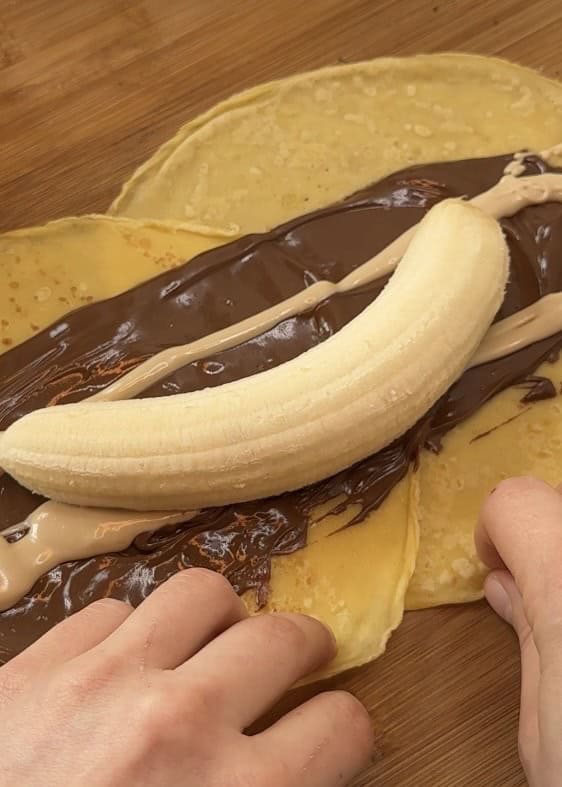 Rolling sushi crepes filled with Nutella and fresh banana slices, prepared on a rustic wooden table, ready for decoration