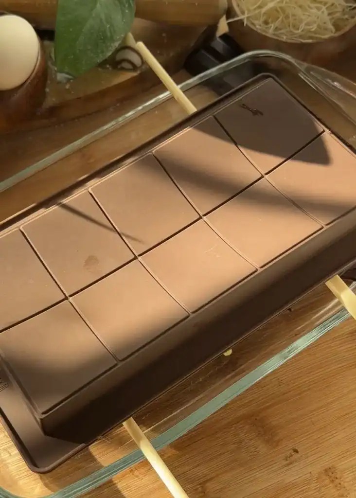 Flipping a chocolate mold over a pan to let excess chocolate drip off, ensuring a smooth finish for homemade Dubai chocolate bars.