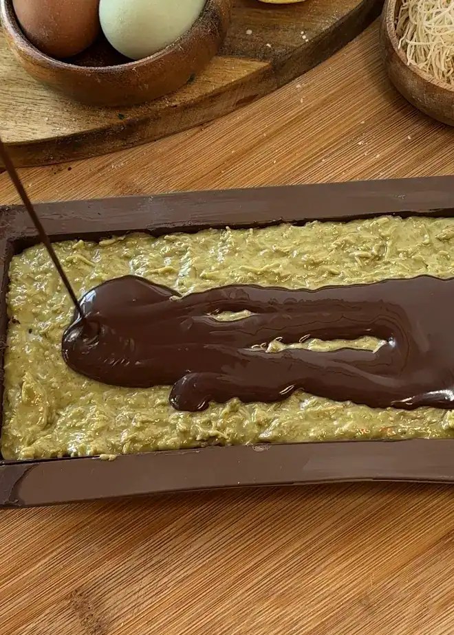 Pouring melted chocolate over a mixture of toasted kataifi, tahini, and pistachio cream in the chocolate mold for homemade Dubai chocolate bars.
