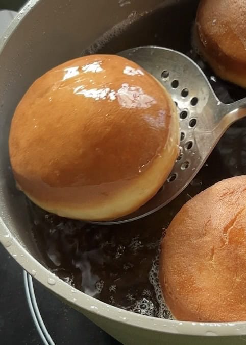 Frying donuts in a cooking pot with hot oil, turning golden brown, to make easy strawberry cheesecake stuffed donuts.