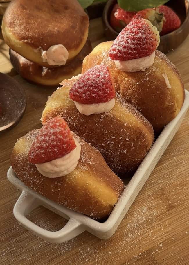 Fluffy strawberry cheesecake stuffed donuts with fresh strawberries on top, coated in sugar, showcasing their delicious filling.