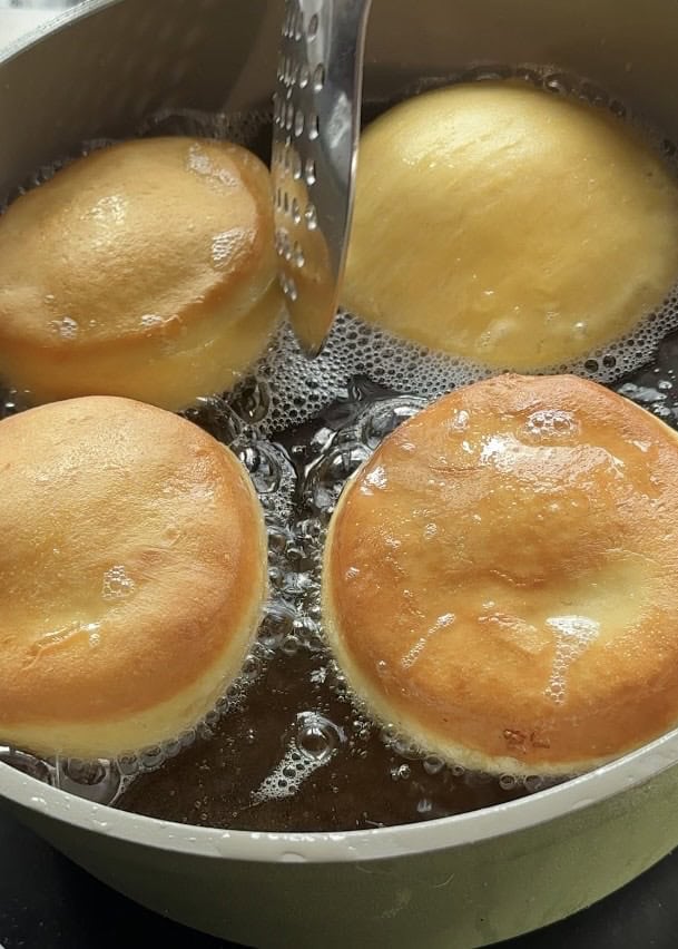 Frying donuts in a cooking pot with hot oil, turning golden brown, to make easy strawberry cheesecake stuffed donuts.