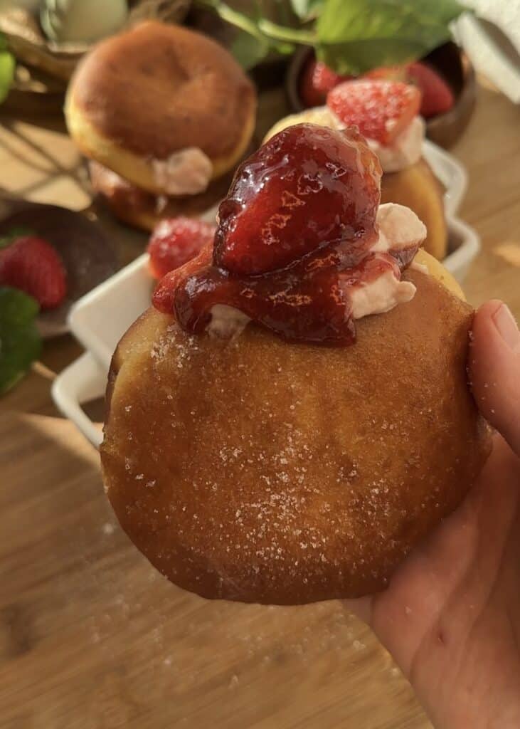 Easy strawberry cheesecake stuffed donuts, filled with strawberry cheesecake, topped with a fresh strawberry, strawberry jam, and dusted with sugar.