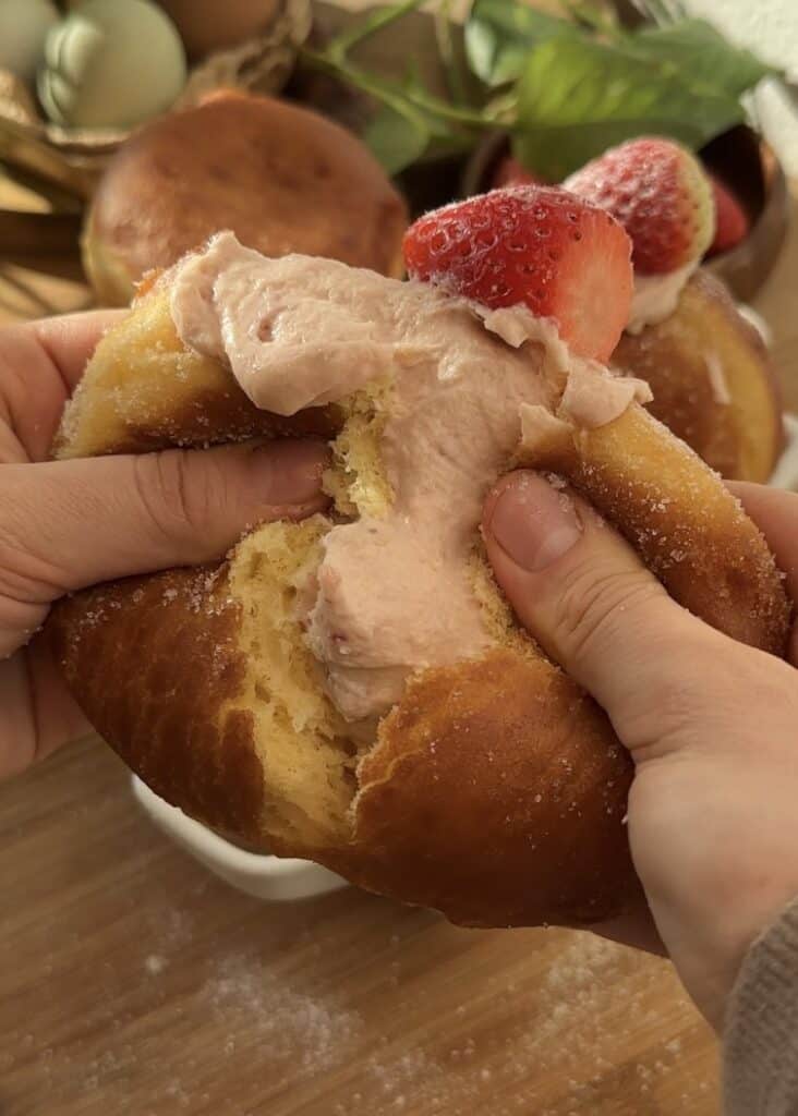 Easy strawberry cheesecake stuffed donuts, cut in half to reveal the creamy strawberry cheesecake filling, topped with a fresh strawberry and coated in sugar.