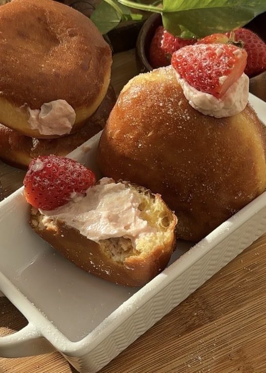 Easy strawberry cheesecake stuffed donuts, cut in half to reveal the creamy strawberry cheesecake filling, topped with a fresh strawberry and coated in sugar.