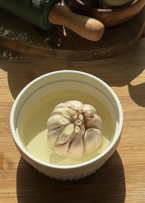Ceramic pot with garlic heads in oil, ready to be confited in the oven for garlic butter filling for buttery cheese garlic rolls.