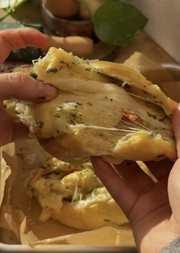 A buttery cheese garlic roll split in half, revealing its soft, fluffy texture with melted, bubbly mozzarella cheese and rich garlic butter inside.