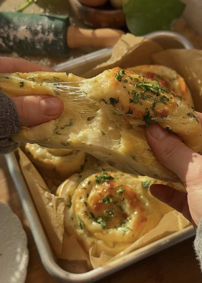 A buttery cheese garlic roll split in half, revealing its soft, fluffy texture with melted, bubbly mozzarella cheese and rich garlic butter inside.
