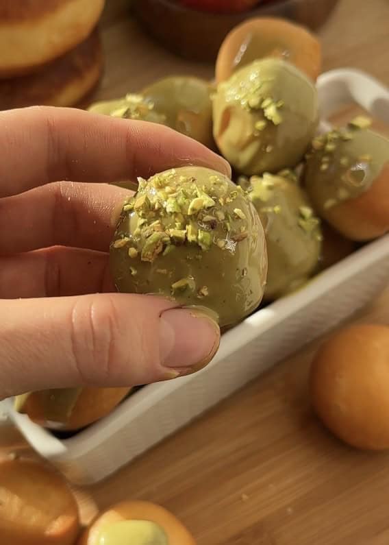Close-up of pistachio donut holes made with sweet dough, fried to perfection, and glazed with creamy pistachio butter, topped with crunchy pistachios for extra texture