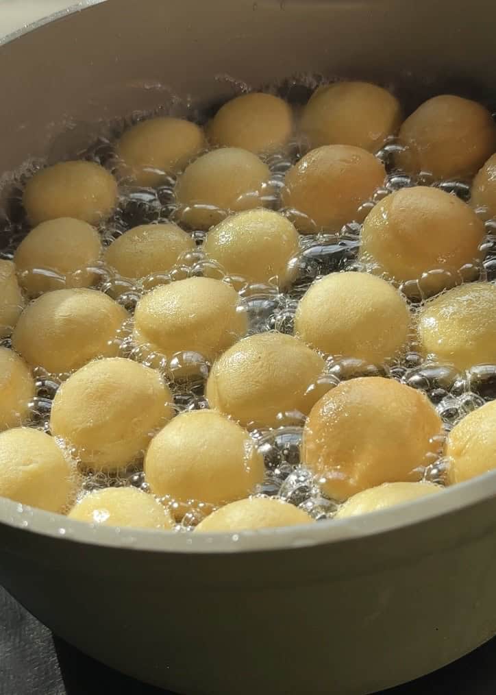 Donut holes frying in hot oil, turning golden brown and becoming perfectly fluffy, ready to be glazed and topped with pistachio butter and crunchy pistachios