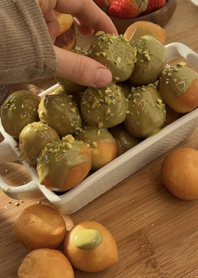 Close-up of pistachio donut holes made with sweet dough, fried to perfection, and glazed with creamy pistachio butter, topped with crunchy pistachios for extra texture