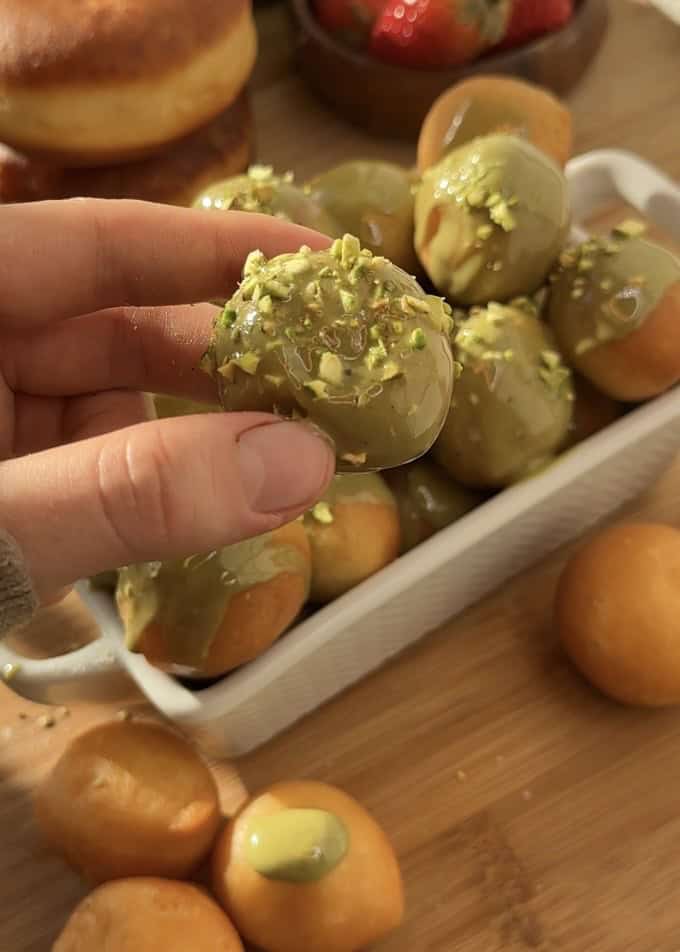 Close-up of pistachio donut holes made with sweet dough, fried to perfection, and glazed with creamy pistachio butter, topped with crunchy pistachios for extra texture