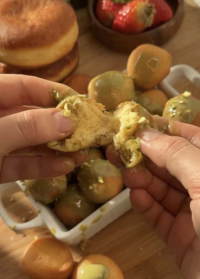 Close-up of opened pistachio donut holes revealing a fluffy interior, glazed with creamy pistachio butter and topped with crunchy pistachios for added texture