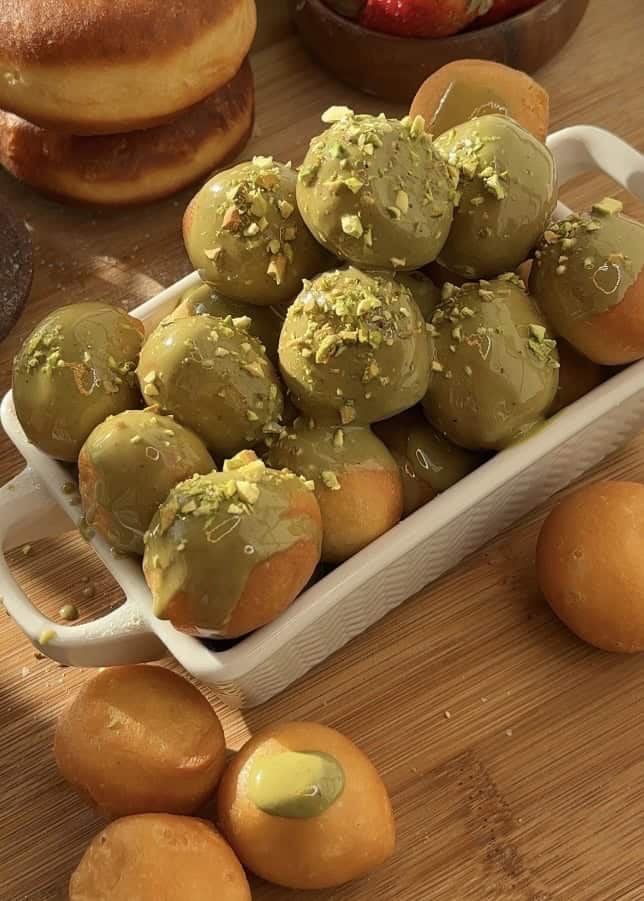 Close-up of pistachio donut holes made with sweet dough, fried to perfection, and glazed with creamy pistachio butter, topped with crunchy pistachios for extra texture