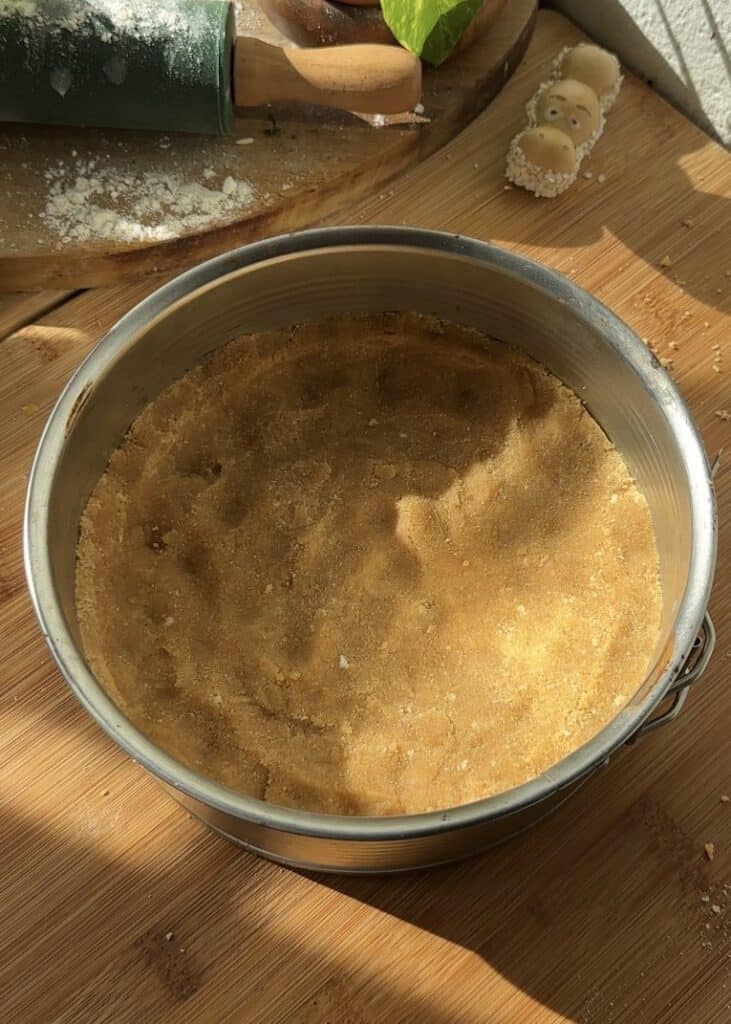 Pressing the cookie crust into a greased mold to create the perfect base for Happy Hippo No-Bake Cheesecake, ready to be filled with creamy hazelnut cheesecake and Kinder-filled layers.